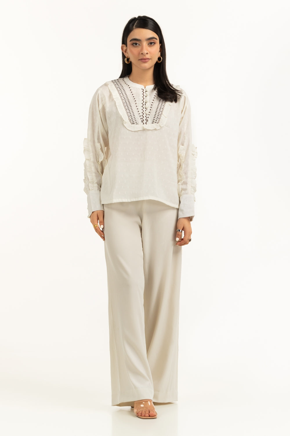 Woman wearing a white blouse with lace details and beige pants on a white background